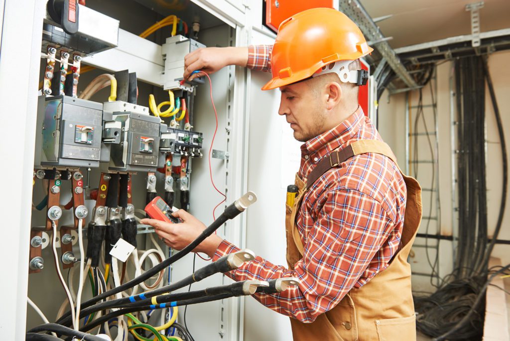 man in overalls wearing orange hard hat repairing furnace