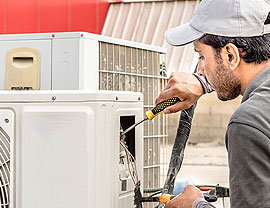 man in gray shirt and gray hat holding yellow screwdriver performing furnace repair