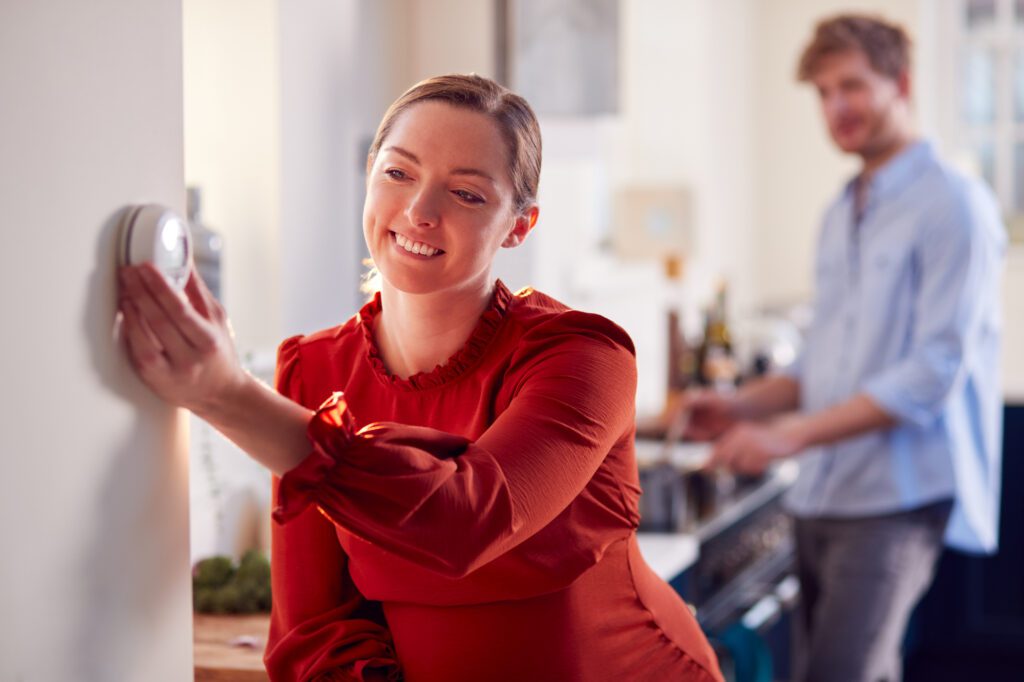 young woman wearing red shirt in kitchen adjusting thermostat