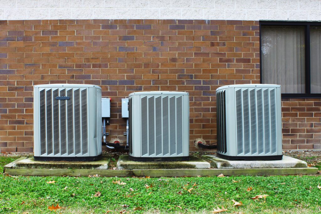 three hvac units against brick wall with window