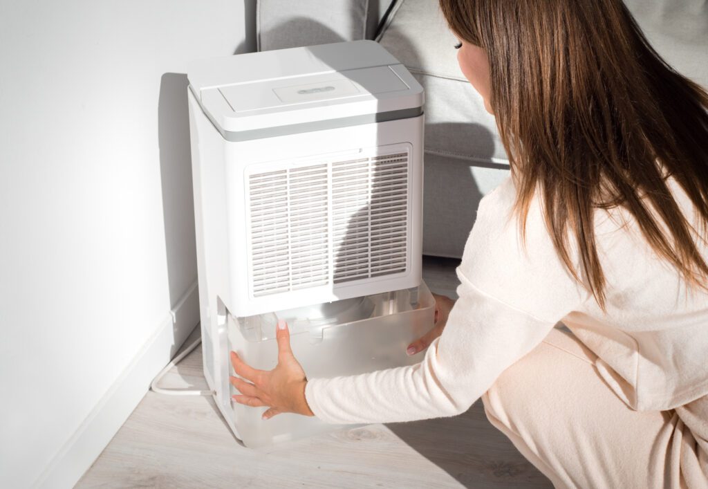 Woman changing water container in air dryer, dehumidifier, humidity indicator. Humid air at home. Fresh air at home. 