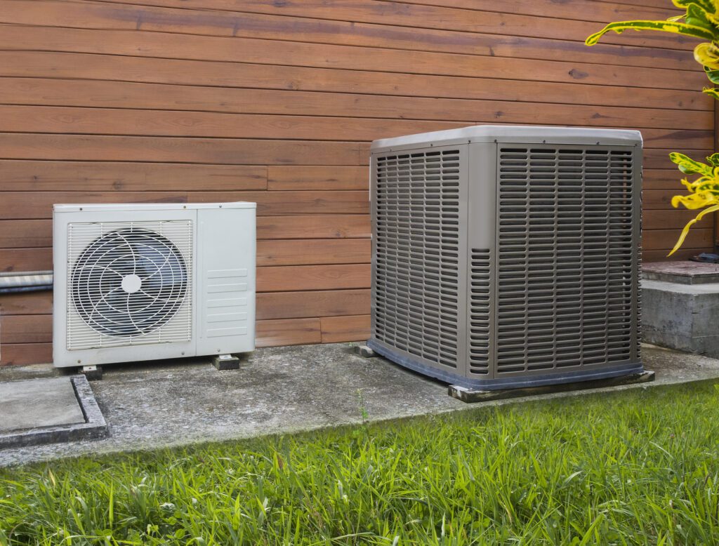 two hvac heat pumps sitting on concrete pad next to home