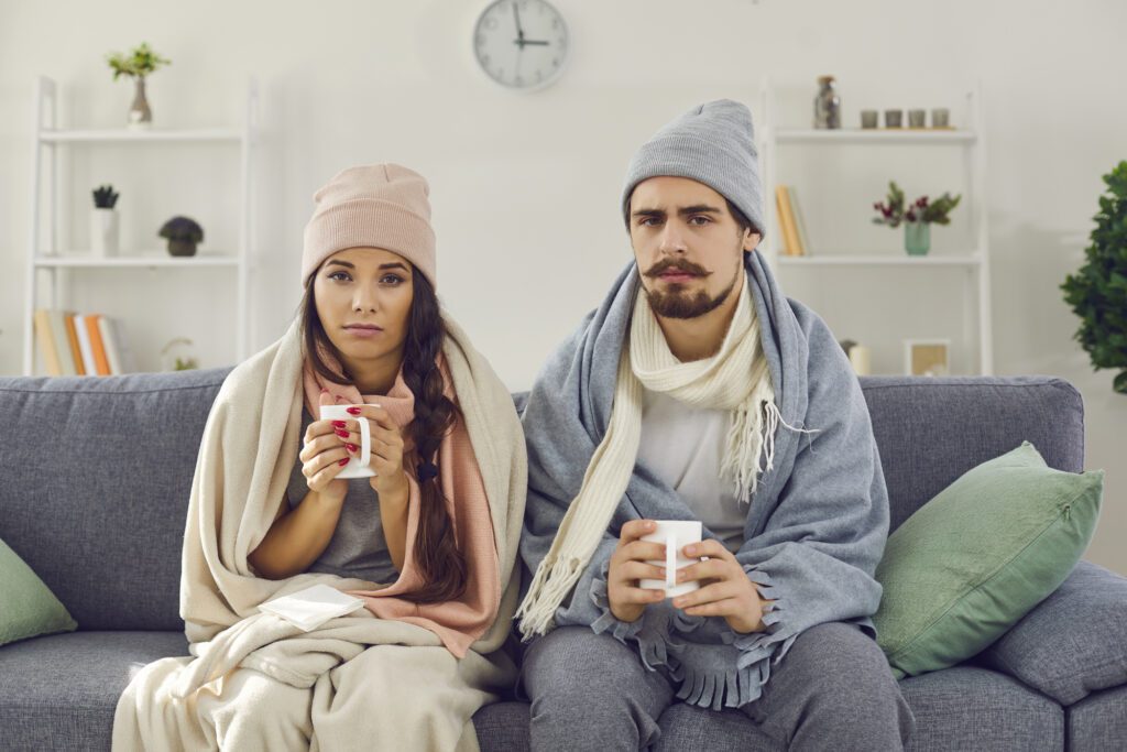young couple sitting on couch holding warm drinks because furnace isn't big enough